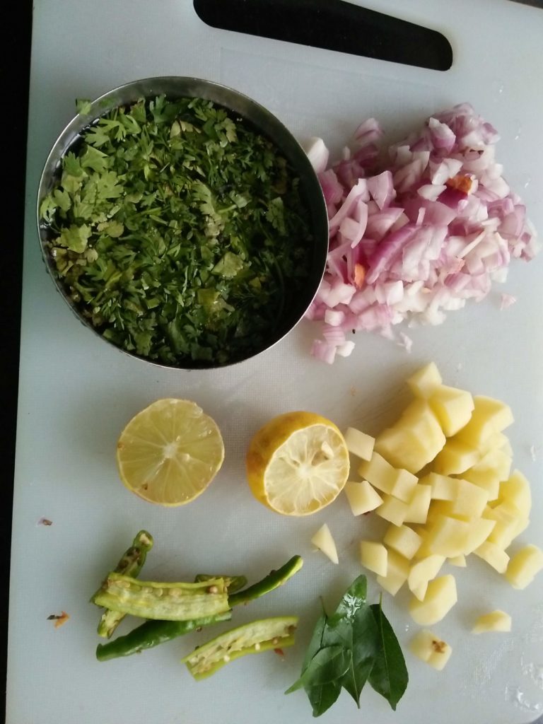 ingredients used for making Poha. Chopped onions, Potatoes, coriander, curry leaves, green chillies, lemon.